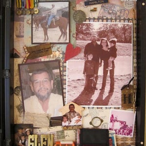Könnte beinhalten: Ein schwarzer Schattenfugenrahmen mit einer Collage aus Familienfotos, Medaillen, einem kleinen orangefarbenen Spielzeugbus, einem weißen Spielzeugauto und dem Wort GLEN in Goldbuchstaben. Das Display enthält Papier-Ephemera, ein rotes Herz und den Text Morena's Corner.