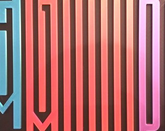 May include: A rectangular wall art piece with the words "STAY GOOD PANIC!" in large, stylized letters. The letters are in shades of blue, red, and purple against a black background. The artwork is mounted on a light-colored wall.
