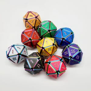 May include: A collection of nine multi-faceted polyhedral dice featuring a metallic iridescent finish on the edges. Each die displays a distinct solid color including orange, green, blue, yellow, white, black, purple, and red with engraved numbers.