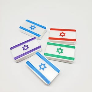 May include: Five rectangular objects with the Israeli flag design. Each object has a white background with a Star of David in the center and colored borders in blue, red, green, purple, and blue. The objects are arranged on a white surface.