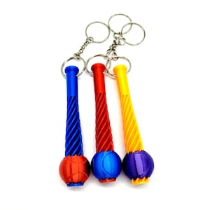 May include: Three colorful keychains with a unique design. Each keychain features a twisted, cylindrical handle in blue, red, and yellow, connected to a spherical base. The bases are in complementary colors, including orange, blue, and purple. The keychains are attached to silver key rings.
