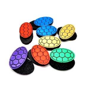 May include: A collection of colorful hair accessories. Each accessory features a turtle shell design in various colors, including red, blue, yellow, green, and purple, set on a black base. The accessories are arranged on a white background.