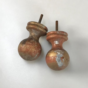 May include: Two vintage furniture legs with a ball-shaped base and a threaded bolt. The legs are painted in shades of gold, copper, and brown, with some areas showing wear and tear. These decorative legs are suitable for a small table or chair.