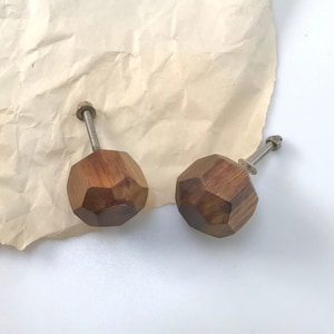 May include: Two wooden cabinet knobs with a geometric design. The knobs are brown and have a silver screw.