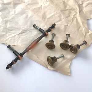 May include: Five antique cabinet knobs with a brass finish. Four of the knobs are round with a small screw on the top. One knob is a longer, rectangular pull with a brown and black finish.