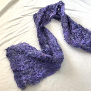 May include: A long, flowing scarf in shades of lavender and gray. The scarf has a textured, almost bubbly appearance, with a loose weave. The fabric appears soft and lightweight, suitable for adding a touch of color and warmth.