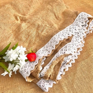 May include: A brown burlap fabric tablecloth with a white lace trim. The tablecloth is folded and a single red strawberry is visible.