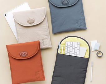 May include: Four different coloured padded laptop sleeves with a small embroidered bear on each. The sleeves are beige, blue, black, and orange. The black sleeve is open and has a keyboard and other accessories inside.