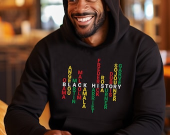 May include: Black hoodie with a red, green, and yellow design featuring a word search puzzle with the words "Black History" in the center. The puzzle includes names of important figures in Black history, such as Martin Luther King Jr., Frederick Douglass, and Sojourner Truth.