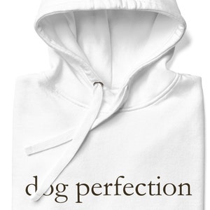 May include: White hooded sweatshirt with the text "dog perfection" and a definition of the word. The definition reads: /dawg/ per-fek-shuhn/ noun a perfect embodiment or example of the etiquette, physicality, and charm of a Canis familiaris.
