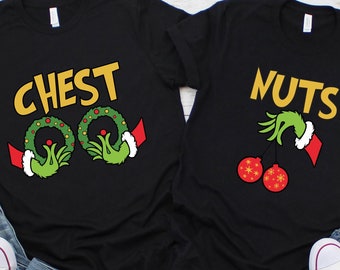 Puede incluir: Dos camisetas negras con gráficos navideños. Una camiseta dice "CHEST" con coronas verdes tipo Grinch. La otra dice "NUTS" con una mano tipo Grinch sosteniendo adornos rojos. Zapatillas blancas y vaqueros azules en primer plano.