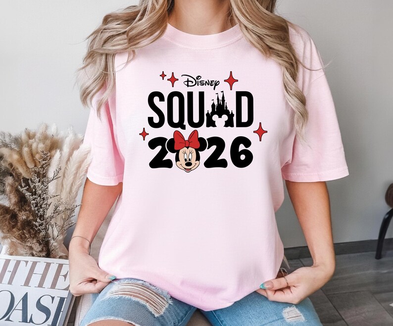 A woman wearing a pink t-shirt with a Disney-themed design, including Minnie Mouse and a castle.