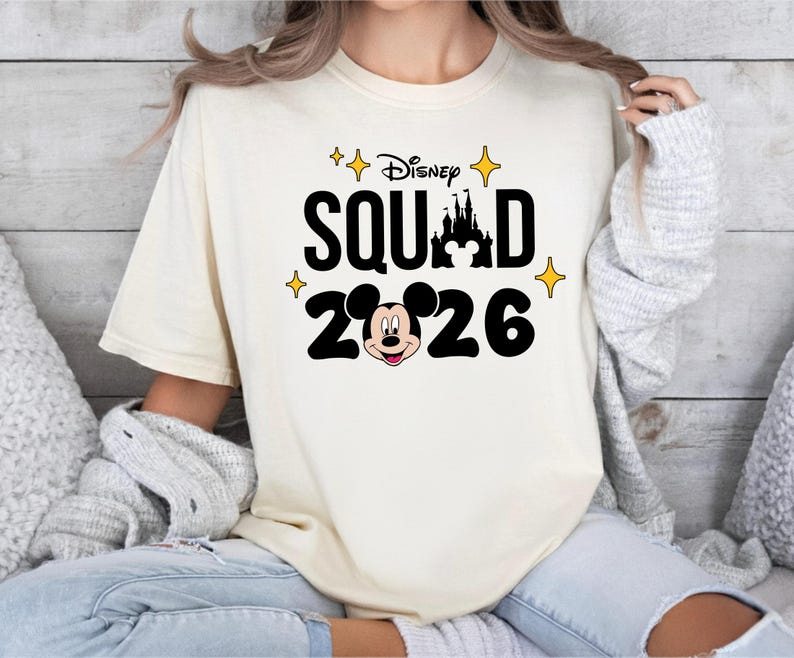 A woman wearing a white t-shirt with a Disney Mickey Mouse graphic and the text "Disney SQUAD 2026" printed on it.
