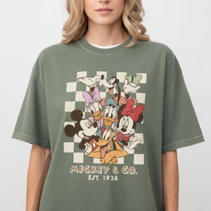 A woman wearing a green t-shirt with a graphic of Disney characters and text below the image.