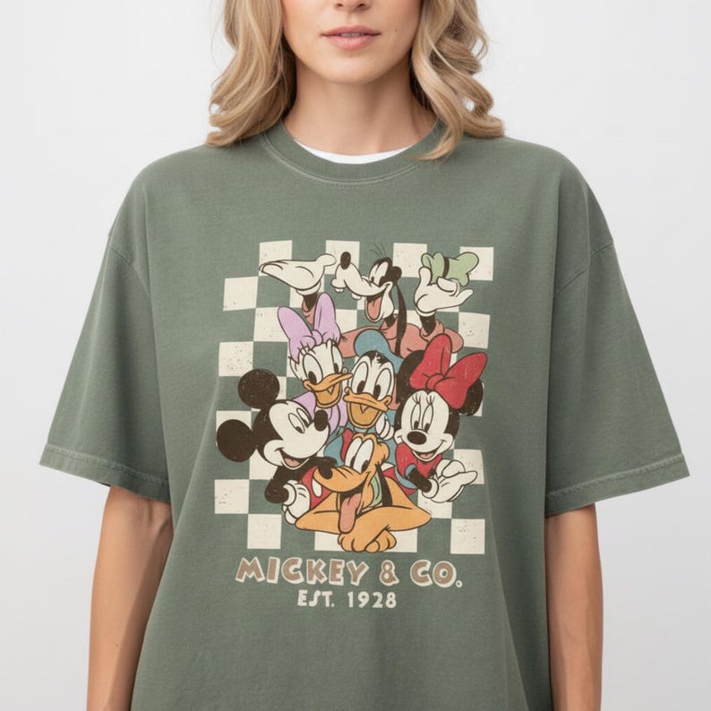A woman wearing a green t-shirt with a graphic of Disney characters and text below the image.