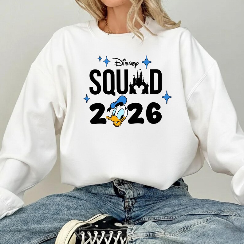 A person wearing a white sweatshirt with a Disney-themed design and text printed on it.
