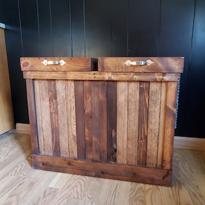 May include: A wooden storage bin with two compartments, each with a metal handle. The bin is made of reclaimed wood and has a rustic look.