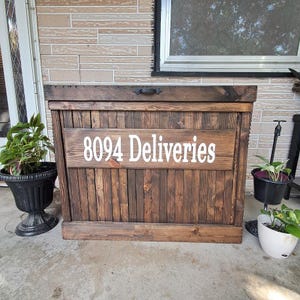 May include: A dark brown wooden box with a hinged lid and a black metal handle. The box has a white sign on the front that says "8094 Deliveries".