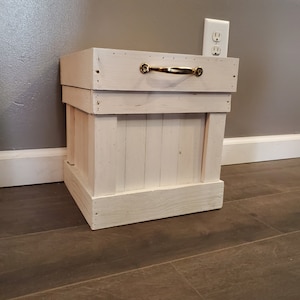 May include: White wooden storage box with a gold metal handle. The box is sitting on a wood floor.