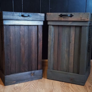 Pu&ograve; includere: Due bidoni della spazzatura in legno con maniglie e catene in metallo nero. I bidoni sono tinti in un colore marrone scuro e grigio.