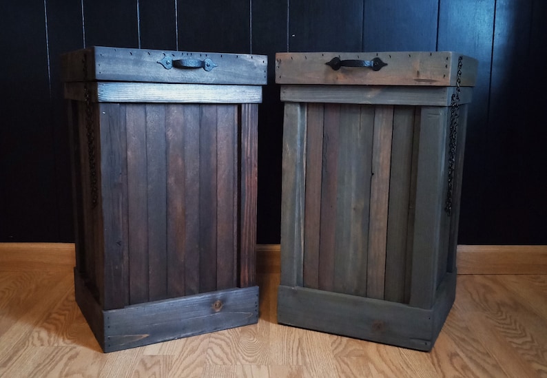Pu&ograve; includere: Due bidoni della spazzatura in legno con maniglie e catene in metallo nero. I bidoni sono tinti in un colore marrone scuro e grigio.