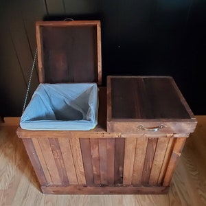 May include: A wooden trash can with two compartments, one with a hinged lid and the other with a removable lid. The trash can is made of reclaimed wood and has a rustic finish.