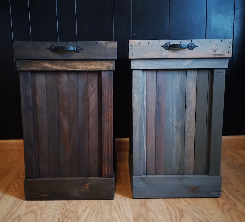 Pu&ograve; includere: Due bidoni della spazzatura in legno con maniglie in metallo nero. I bidoni della spazzatura sono realizzati in legno riciclato e hanno una finitura rustica.