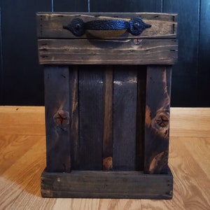 May include: A dark brown wooden storage box with a black metal handle. The box has a rustic, distressed look and is made of reclaimed wood.