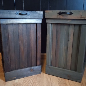 Pu&ograve; includere: Due bidoni della spazzatura in legno con maniglie in metallo nero. I bidoni della spazzatura sono realizzati in legno riciclato e hanno una finitura rustica. Un bidone della spazzatura &egrave; marrone scuro e l'altro &egrave; grigio-verde chiaro.