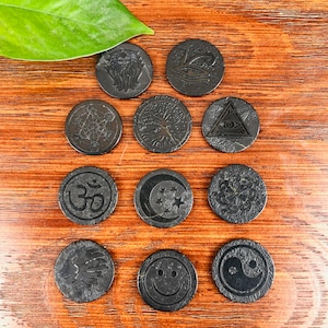 Pode incluir: Doze  costas de pedra redonda preta com vários desenhos, incluindo uma árvore, um olho, um símbolo, uma lua e um símbolo yin yang.