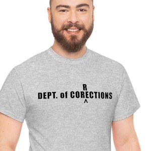 Peut inclure: Un t-shirt gris chiné avec un texte noir qui dit "DEPT. OF CORRECTIONS" avec un "R" et un "A" stylisés dans le texte.