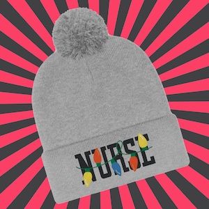 May include: A light grey beanie hat with a matching pom-pom. The word "NURSE" is embroidered in black, with a string of colourful Christmas lights. The background features a red and black striped pattern.