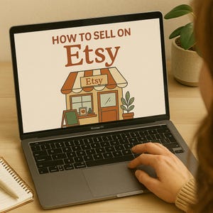 May include: A laptop displaying a screen with the text "HOW TO SELL ON Etsy" above an illustration of an Etsy shop. A hand is using the trackpad. A notebook and pen are visible on the desk.