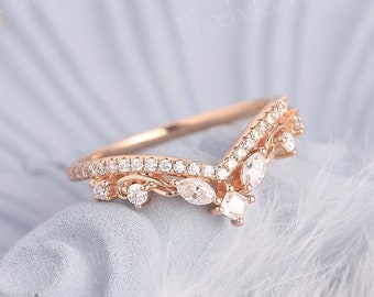May include: A delicate rose gold ring with a V-shaped design featuring a row of small diamonds and three larger pear-shaped diamonds.
