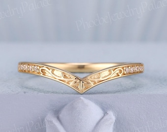 Puede incluir: Un anillo dorado en forma de V con un patrón de hojas grabado a lo largo de la banda y pequeñas piedras transparentes incrustadas en los bordes exteriores. El metal tiene un acabado pulido y el diseño forma una punta en el centro.