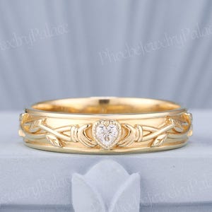 May include: A gold wedding band with a delicate vine design and a small heart-shaped diamond in the center.
