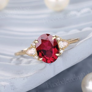 May include: A gold ring featuring a large oval ruby gemstone and three smaller pear-shaped diamonds. The ring is displayed against a white backdrop.