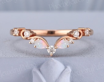 May include: A delicate rose gold wedding band with a V-shaped design. The band is adorned with small round diamonds and two pear-shaped opals.