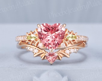May include: A rose gold engagement ring set with a large heart-shaped pink gemstone as the centerpiece. The ring is flanked by smaller green and white gemstones, with a matching band. The design includes intricate details and a delicate, romantic aesthetic.