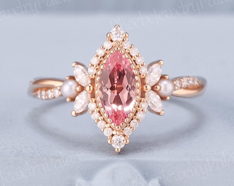 May include: A rose gold ring featuring a marquise-cut pink gemstone at the center, surrounded by a halo of small diamonds. The ring has delicate side accents with pearls and smaller gemstones, and a twisted band.