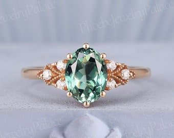 May include: A rose gold engagement ring with an oval green gemstone surrounded by smaller diamonds. The ring has a delicate, vintage-inspired design with intricate details.