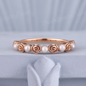 May include: A delicate rose gold band ring with a row of small white pearls set in rose gold rose motifs.