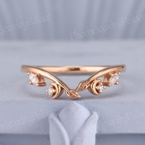 May include: A delicate rose gold wedding band with a leaf design and small diamonds. The band is curved to fit the shape of a finger.