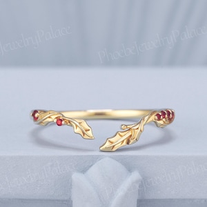 May include: A gold open-style ring featuring a delicate leaf motif along the band. The design includes small, round, red gemstones embedded within the metal leaves on both ends of the opening, creating a nature-inspired look with a polished finish.