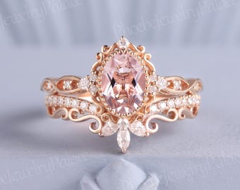Könnte beinhalten: Ein Verlobungsring aus Roségold mit einem großen ovalen Morganit-Edelstein, der von kleineren Diamanten umgeben ist. Der Ring hat ein zartes, verziertes Design mit filigranen Details.