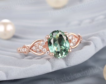 May include: A rose gold ring with a green oval gemstone surrounded by smaller diamonds. The ring has a delicate, twisted band.