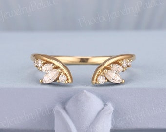 Puede incluir: Un anillo abierto de oro con dos grupos simétricos de piedras transparentes de talla marquesa y redonda. La banda es de oro pulido y el diseño deja un espacio en el centro, mostrando una delicada disposición de gemas blancas brillantes.