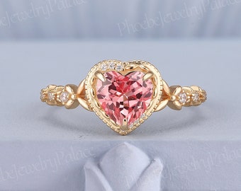 Könnte beinhalten: Ein goldener Herzring mit einem rosafarbenen Edelstein, der von kleineren Diamanten umgeben ist. Der Ring hat ein zartes Blumenmuster auf der Band.