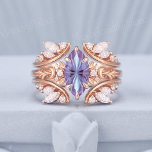 May include: A rose gold engagement ring set featuring a marquise-cut, light purple gemstone. The ring is flanked by leaf-shaped accents and small, clear gemstones. The band has a delicate, ornate design. The text "PhoebeJewelryPalace" is visible.