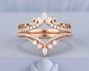 May include: A rose gold ring with a delicate crown design featuring marquise-shaped and round clear stones. The ring has a delicate floral design with small pearls.